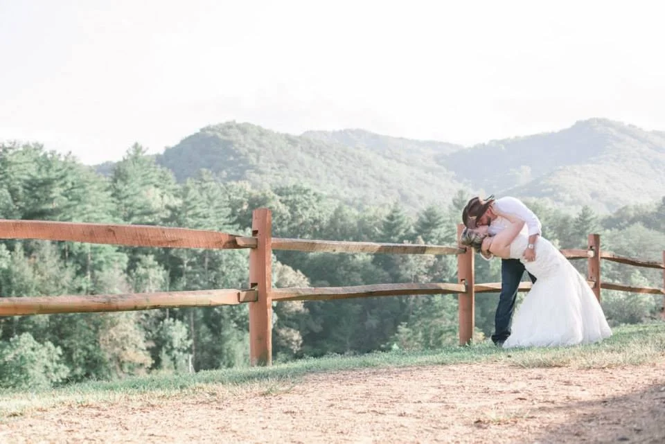 Wedding couple kissing by rustic fence with Smoky Mountains views at Moose Hollow Lodge in Pigeon Forge near Dollywood