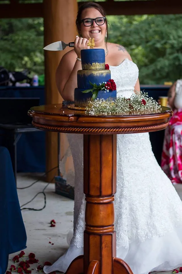 Bride with wedding cake on wooden table at outdoor reception at Moose Hollow Lodge in Pigeon Forge near Smoky Mountains