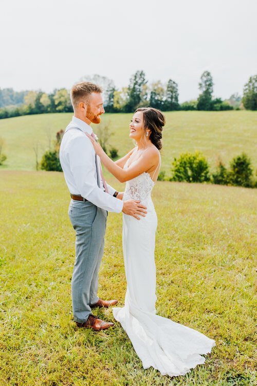 Couple in wedding attire stands in a grassy field at Moose Hollow Lodge, looking at each other.