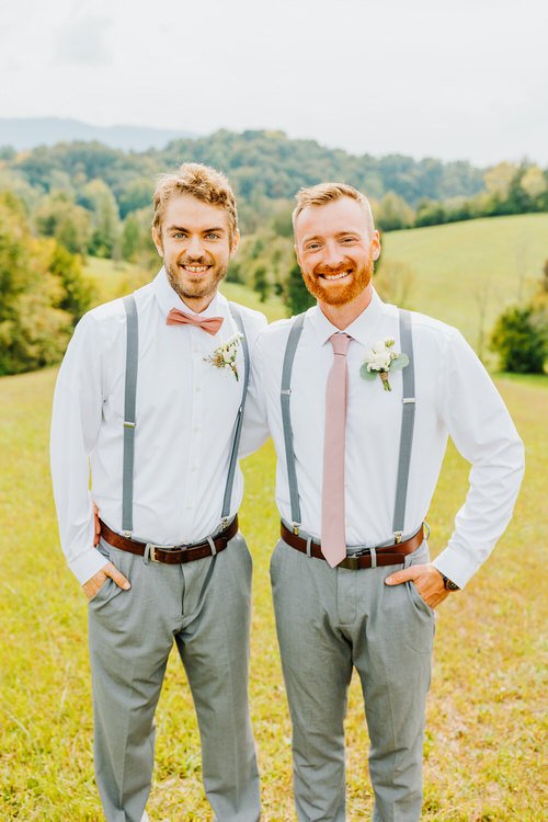 Two men in white shirts, grey pants, peach ties, and grey suspenders in a field. Green hills, mountains in background....