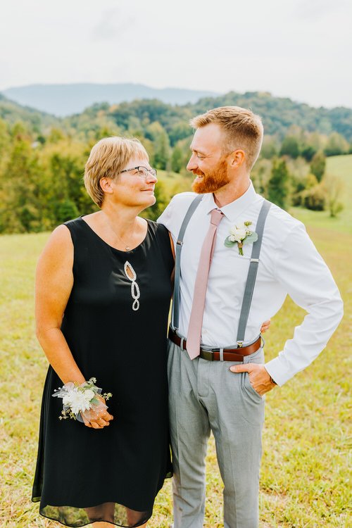 Woman in black dress with white corsage and man in white shirt, suspenders, tie, boutonniere, in grassy field with...