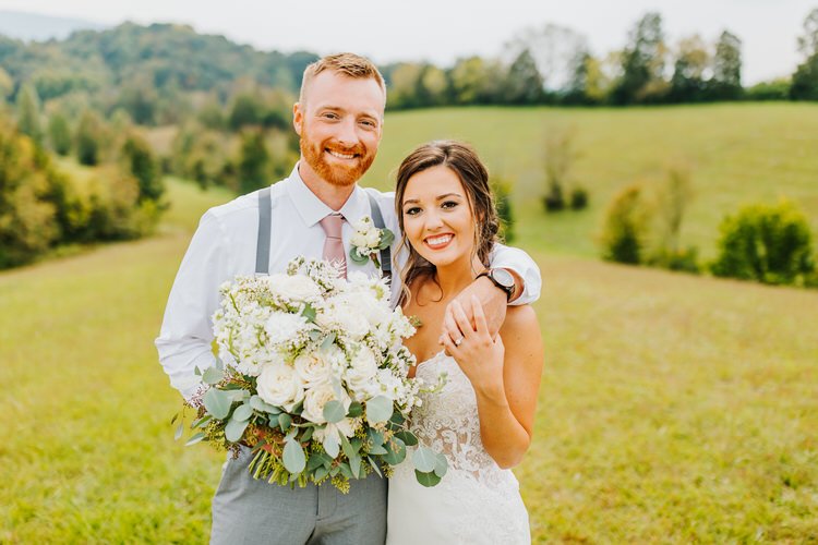 Wedding couple poses with white floral bouquet at Moose Hollow Lodge, TN. Groom in suspenders, bride in lace dress, green...