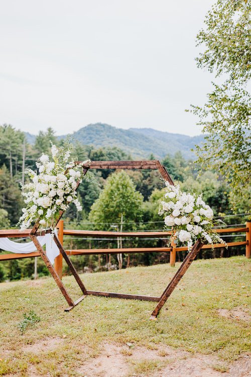 Hexagonal wooden wedding arch decorated with white flowers and white drapery on a grassy slope at Moose Hollow Lodge.