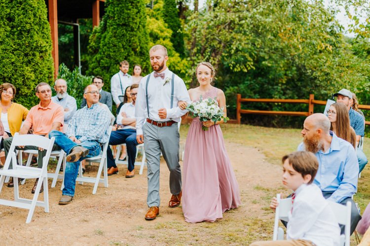 A man and woman walk arm-in-arm down an outdoor wedding aisle past seated guests. Moose Hollow Lodge setting.