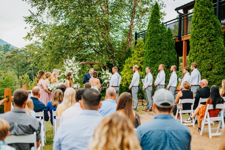 Outdoor wedding ceremony at Moose Hollow Lodge. Bride, groom, wedding party, guests, floral arch, mountain view, trees.
