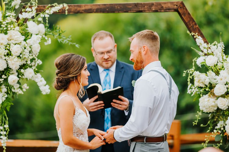 Bride and groom holding hands during outdoor wedding ceremony with officiant and floral arch at Moose Hollow Lodge,...
