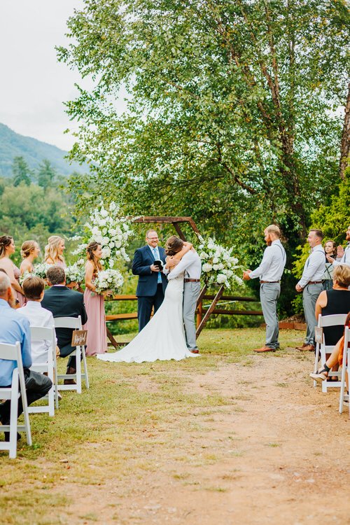 Wedding ceremony at Moose Hollow Lodge: bride and groom embrace under a floral arch with mountains, guests, and bridal party.
