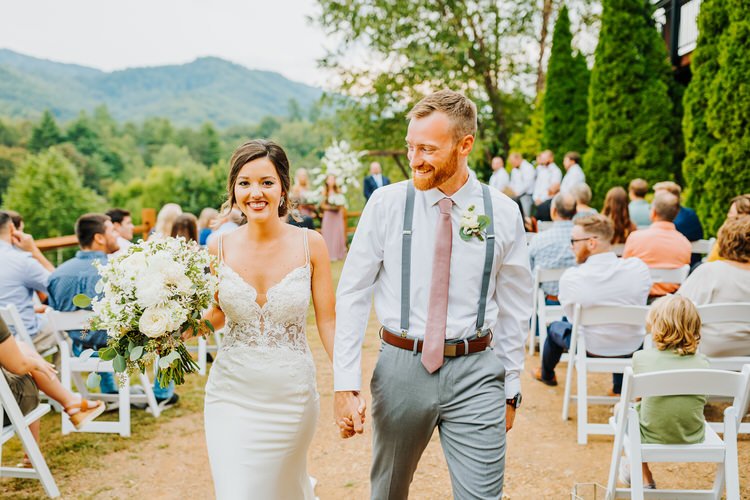 Bride and groom walk down an outdoor aisle, holding hands, with guests and Smoky Mountains behind them at Moose Hollow Lodge.