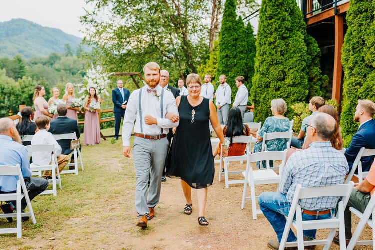 Man walking arm-in-arm with a woman down an outdoor wedding aisle. Guests seated, bridesmaids in background. Moose Hollow...