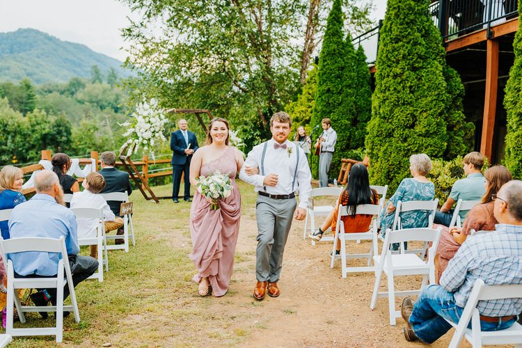 Couple walks down outdoor aisle past seated guests at a Moose Hollow Lodge wedding. Mountains and trees in background.