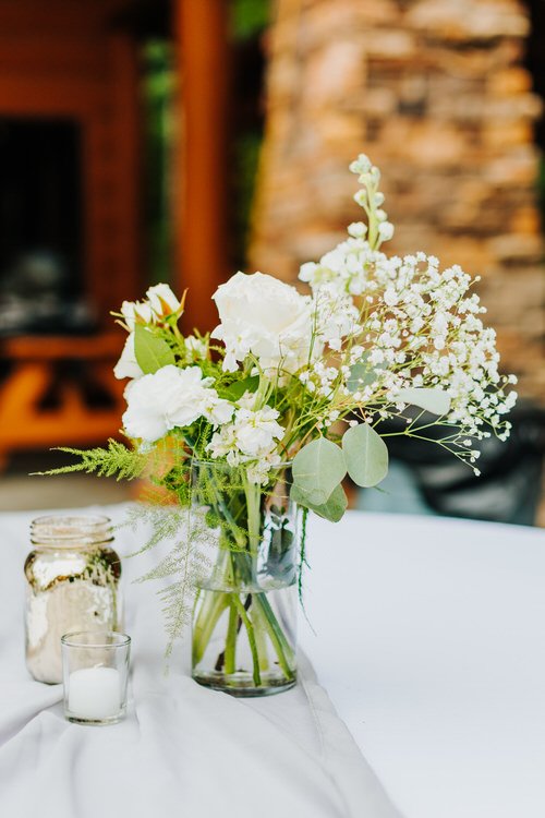 White floral centerpiece in glass vase with roses and greenery on white table. Mercury glass jar and candle. Moose Hollow...