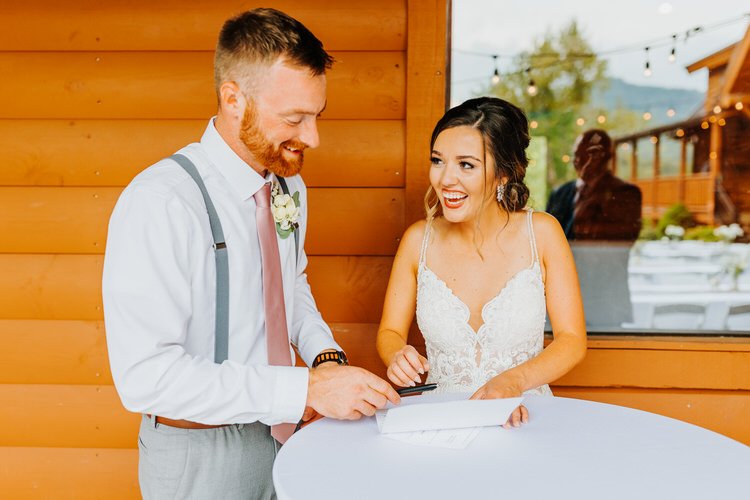 Bride and groom signing documents at white table outside Moose Hollow Lodge. String lights and mountains in background.