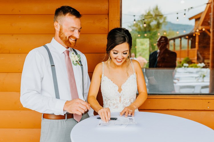 Bride signing documents with groom by a wooden wall and window with mountain reflections at Moose Hollow Lodge.