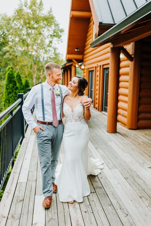 Bride and groom walking on a wooden deck next to a log cabin at Moose Hollow Lodge with green trees in the background.