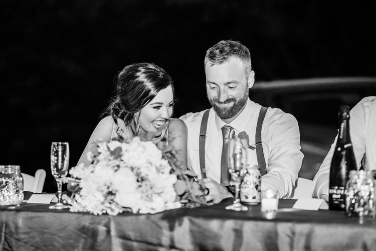 Black and white photo of a smiling woman and man at a reception table with a large floral centerpiece and drinks.
