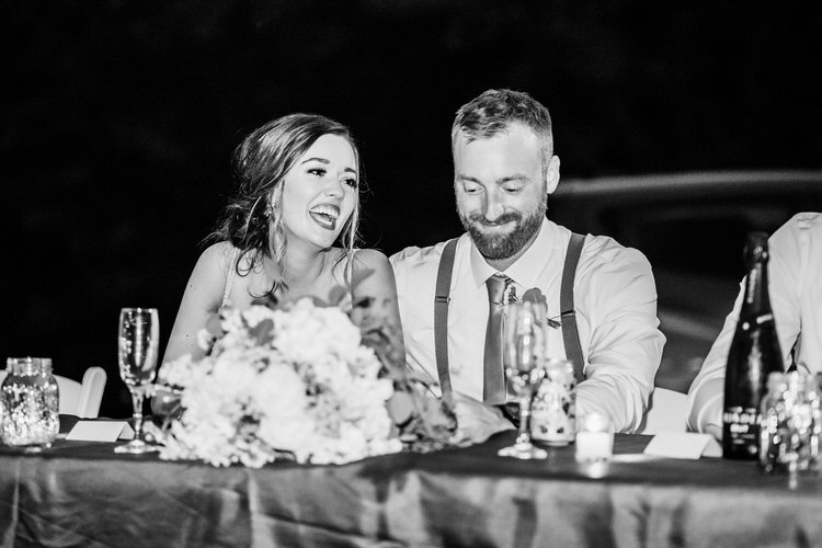 Couple laughing at reception table with floral centerpiece, champagne flutes, and decor in a black and white photo.