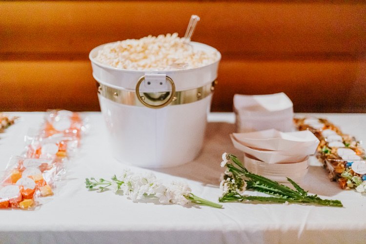 White table with a bucket of popcorn, individual bags of orange candies, and small white flowers. Warm wood background.
