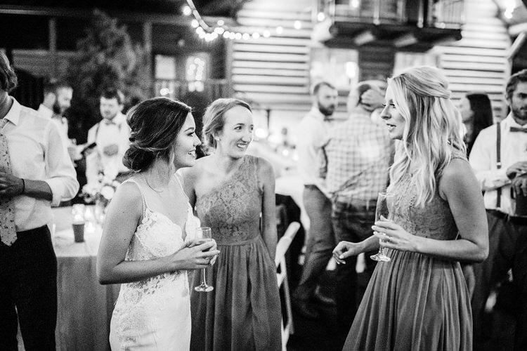 Bride and two guests talking at a rustic wedding reception at Moose Hollow Lodge with string lights overhead.