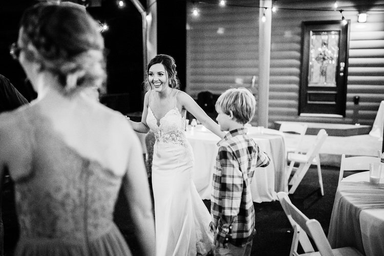 Bride in a white dress smiles at a boy in a plaid shirt at an outdoor nighttime reception with string lights at Moose...
